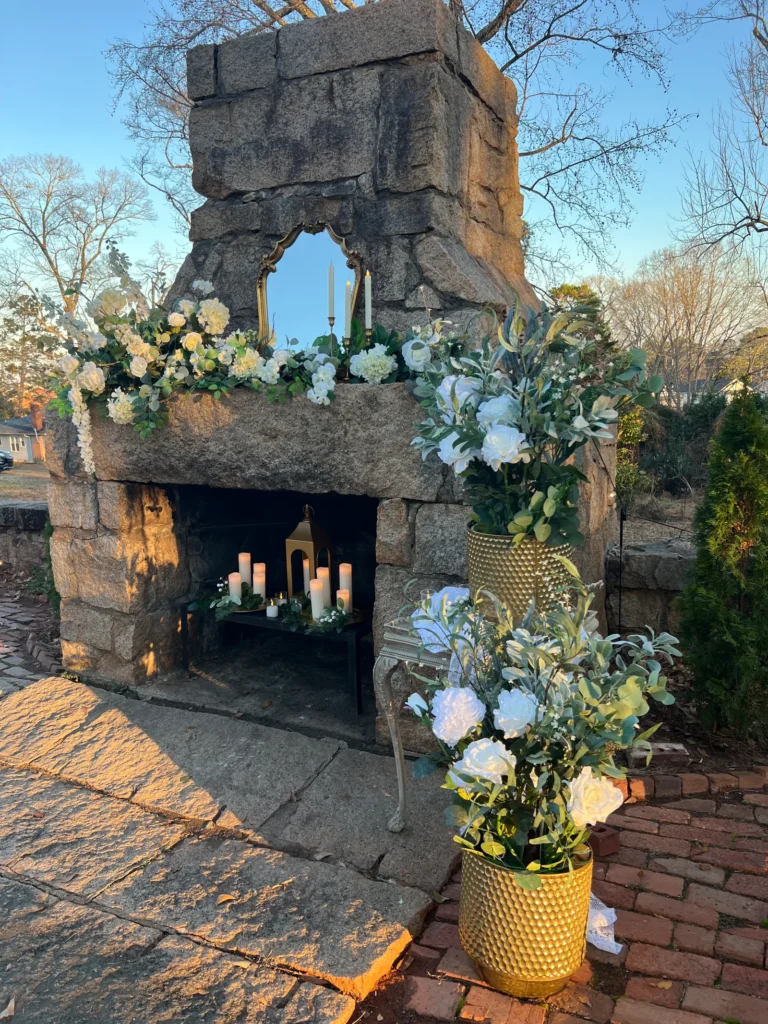 stone outdoor shrine with a mirror, white floral arrangements, and lit candles in a brick and stone alcove.